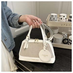 Detail of beige canvas tote with white leather trim and round luggage tag detail