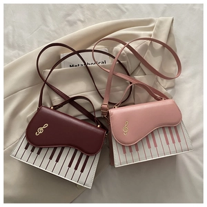 Detail of piano keyboard print handbags in burgundy and pink with golden music note hardware