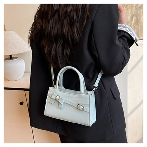 Light blue crossbody bag with bow detail worn by a model in a black blazer suit