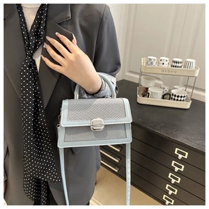 Détail d'un sac bandoulière bleu clair avec rabat tissé et fermoir pivotant en métal argent