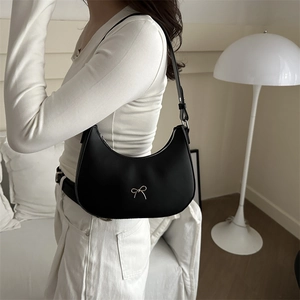 Detail of black leather half-moon shoulder bag featuring a silver metal bow buckle