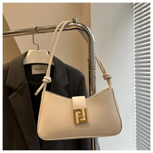 Detail of cream leather shoulder bag featuring a large gold geometric buckle and knotted straps