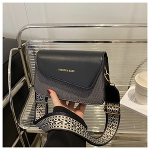 Detail of crossbody bag with wide geometric strap and golden hardware on metallic shelf
