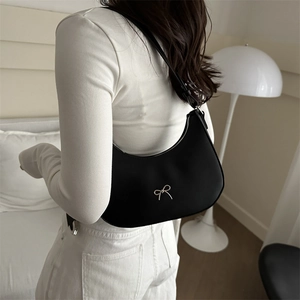Detail of black hobo bag with silver bow buckle worn as shoulder bag in home setting