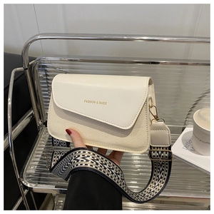 Close-up of cream textured crossbody bag with broad geometric strap and gold hardware