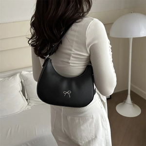 Detail of a black hobo bag with silver bow charm worn by a model in a modern indoor setting