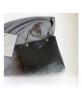 Close-up of black crocodile pattern tote bag with golden chain strap and leather texture