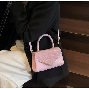 Detail of pink sequined crossbody bag with V-shaped metal trim worn by a model