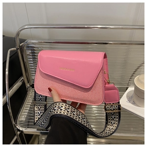 Close-up of pink shoulder bag with smooth flap, woven body and ethnic style wide strap