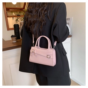 Pink crossbody bag with bow detail and metal hardware shown on a black suit jacket
