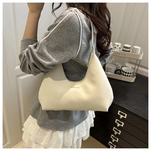 Fashionable half-moon cream shoulder bag with logo detail on model in home setting