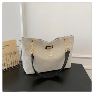 Détail d'un sac cabas en toile avec bandoulière en cuir et pendentif cerf doré sur bois