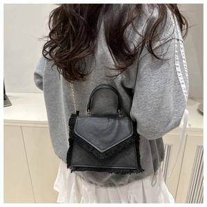 Détail du sac carré en cuir noir avec franges et bandoulière en chaîne dorée à l'épaule