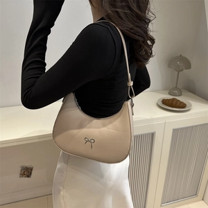 Model wearing a minimalist cream crescent bag with a silver metallic bow detail