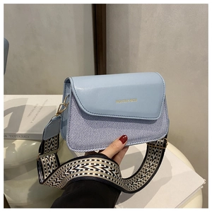 Detail of light blue crossbody bag featuring woven texture and geometric patterned wide strap