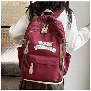 Detail of burgundy nylon backpack featuring white SJM lettering and khaki zipper pullers