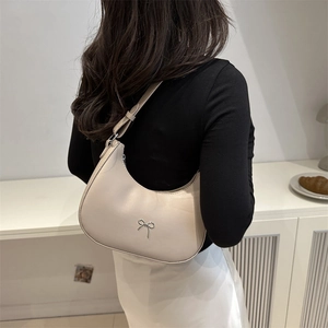 Close-up of a cream crescent shoulder bag with a silver bow detail on a female model