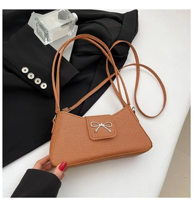 Close-up of brown textured underarm bag with elegant silver bow hardware clasp