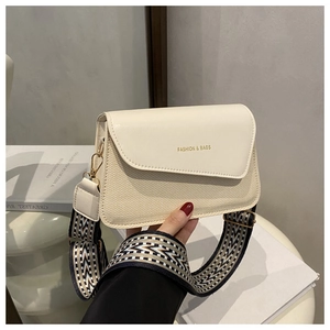 Detail of minimalist beige handbag showing woven texture, wide strap and gold hardware