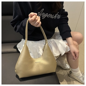 Detail of golden crescent shoulder bag with metallic finish and delicate brand text logo
