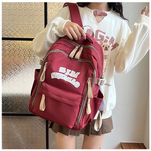 Detail of burgundy nylon backpack featuring multi-zipper layers and white letter printing