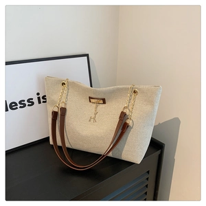 Détail du sac cabas en toile beige avec anses en cuir et pendentif cerf doré élégant