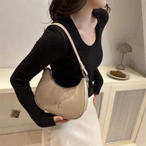 Close-up of beige dumpling bag with silver bow charm and adjustable strap on a model