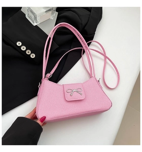Detailed close-up of pink baguette bag with silver metal bow and textured leather