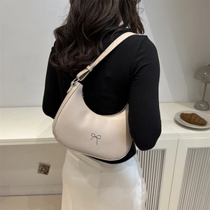 Chic cream white hobo bag with silver bow detail shown on shoulder in a stylish setting