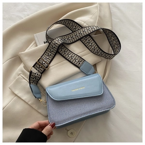 Detail of light blue crossbody bag with woven texture and geometric patterned wide strap