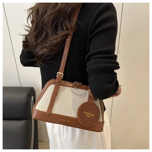 Detail of canvas tote bag with brown leather trim and small round charm on model back