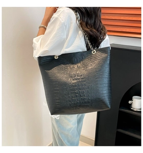 Side view of large black crocodile pattern tote bag with gold chain strap on model