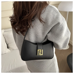 Detailed view of black underarm bag with gold geometric buckle on a model shoulder