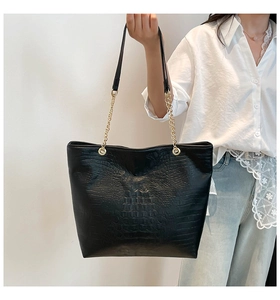 Detail of black crocodile texture tote bag featuring golden metal chain and leather strap