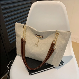 Grand sac cabas en nylon beige avec bandoulières en cuir marron et chaîne dorée sur chaise