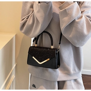 Detail of black glitter crossbody bag with gold V-shaped metal trim and sleek handle