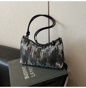 Detail of sequined underarm bag with silver stripes and leather straps on a book