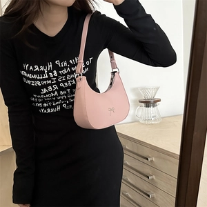 Pink half-moon underarm bag featuring a silver bow detail held by a model in casual wear