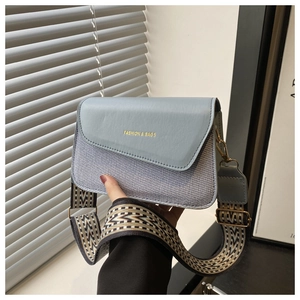 Detail of color-block handbag showing blue leather flap and woven texture body
