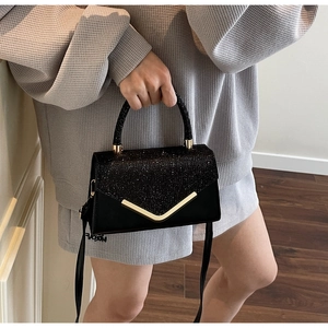 Detail of elegant black rhinestone handbag with golden V-shaped metal hardware and top handle