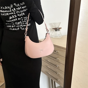 Pink crescent shoulder bag with metallic bow detail styled on a model in black dress