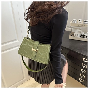 Close-up of green baguette bag with golden H-buckle worn on shoulder by a model