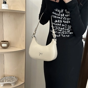 Detail of cream half-moon bag featuring a delicate metal bow and adjustable strap