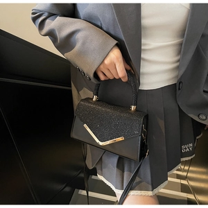 Detail showing elegant black glitter handbag with golden V-shaped trim on model dress