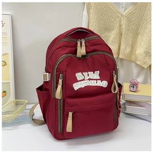 Detail of burgundy nylon backpack with SJM logo surrounded by student lifestyle items