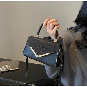 Close-up of a black leather handbag with glitter accents and elegant gold V-shape buckle