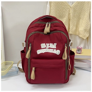 Detailed close-up of maroon nylon backpack featuring white letter patch and functional zippers