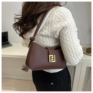 Close-up of dark brown leather crossbody bag featuring gold buckle on white knit sweater