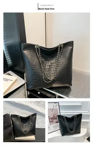 Detail of black crocodile pattern tote bag with golden dual chain shoulder straps