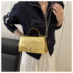 Detailed view of the gold crocodile embossed leather handbag with V-shaped metal buckle